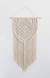 A handmade 100% cotton macrame wall decoration hanging on a white wall.