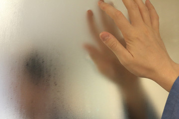 A meditative man with a bathrobe in a bathroom watching himself in a foggy blurry mirror and bringing his hand close to it, in an introspective moment