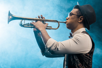 Wall Mural - side view of jazzman playing on trumpet on stage with dramatic lighting and smoke