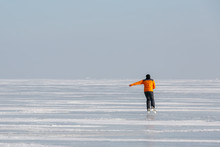 Young Man In An Orange Sweatshirt Alone Skates On The Ice Of A Frozen Sea Bay