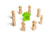© Andrii Yalanskyi - Wooden figurines of people stand around a green house. Search for a new home and real estate. Buying or selling a home. Moving to a new home. Rent or construction. Investments