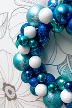 Christmas Wreath Made Of Blue, Navy, Wight Christmas Decoration Balls Hanging On The Wall. White And Silver Flower Background.