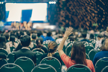 Rear view of Audience in put hand up acton for answer the Speaker question on the stage in the big hall meeting or seminar room, business and education concept