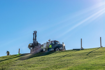 Caucasian male Engineers working and operating a hydraulic telescopic truck mounted auger crane drill rig on a hill on a sunny summer day. Professional team of men hard at work in the field.