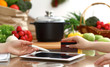 © rogerphoto - Close-up of human hands using tablet or touch pad. Two women in kitchen. Cooking, friendship or online shopping concepts