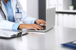 © rogerphoto - Unknown doctor woman typing on laptop computer while sitting at the desk in hospital office. close-up of hands. Physician at work. Medicine and health care concept