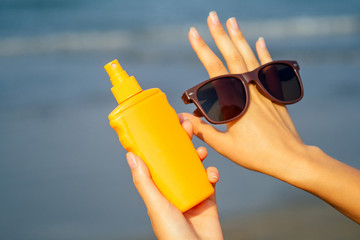 Bottle of sunscreen lotion suncream packaging on the sandy beach sea sky background copy space.Sunglasses on hand palm,oil spa spf vacation on tropical paradise copyspace.Hello summer