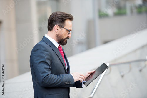 Fotografie, Obraz Profile of concentrated mature manager using a tablet in the street