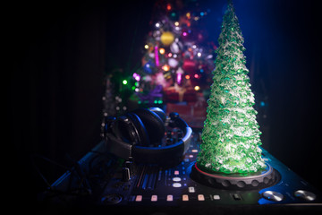 Dj mixer with headphones on dark nightclub background with Christmas tree New Year Eve. Close up view of New Year elements on a Dj table. Holiday party concept.