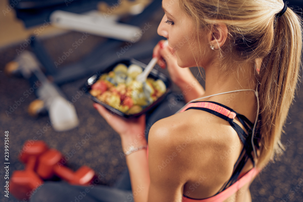 Top view of woman eating healthy food while sitting in a gym. Healthy lifestyle concept. - obrazy, fototapety, plakaty 
