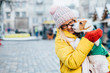© Iryna - Young hipster teen woman in bright casual outfit (knitted hat, red mittens, yellow jacket) holding Jack Russell terrier puppy on her hand, trying to pose, but the dog is licking and chewing her nose