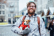 © Iryna - Portrait of funny bearded hipster caucasian man in eyeglasses embracing his Jack russel terrier dog in red jacket, looking at camera and smiling in outdoor winter market square european city.