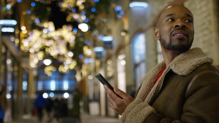 Portrait of handsome black male using his phone outdoors in the city at Christmas