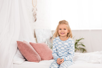 adorable smiling child sitting on bed in morning