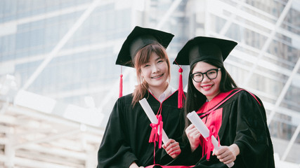 Two girls in black gowns and hold diploma certificate with happy graduated.