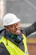 © cineberg - African American engineer wearing yellow protective workwear looking upwards among scaffolding