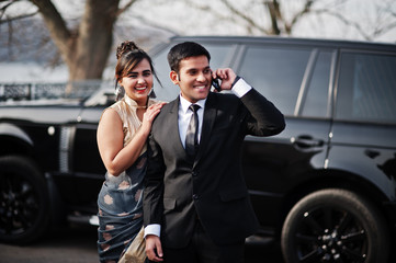 Wall Mural - Elegant and fashionable indian friends couple of woman in saree and man in suit posed against rich black suv car. Guy speaking on mobile phone.