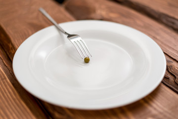 Diet concept. One pea lying on a white plate. Restriction in nutrition.