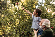 © Yakobchuk Olena - Grandfather holding his granddaughter picking apple from tree