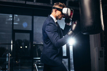 Wall Mural - side view of businessman in suit and virtual reality headset boxing in gym