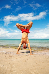 athletic man on beach doing fitness yoga exercise. Acroyoga element for strength and balance.