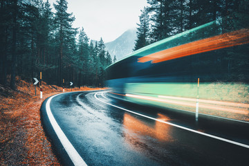 Wall Mural - blurred green bus on the road in autumn forest in rain. perfect asphalt mountain road in overcast ra