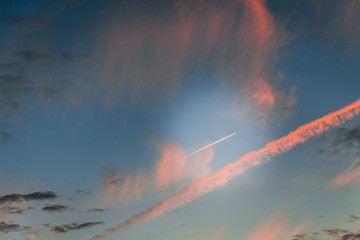 Wall Mural - Dramatic sky with pink stripes. Airplane flying in the sky