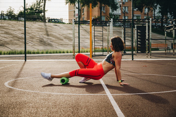 theme sport and rehabilitation sports medicine. Beautiful strong slender Caucasian woman athlete uses foam roller green field street workout to workout to remove pain, stretch and massage muscles