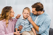 © LIGHTFIELD STUDIOS - happy parents sitting on sofa and touching with fingers nose of son in apartment