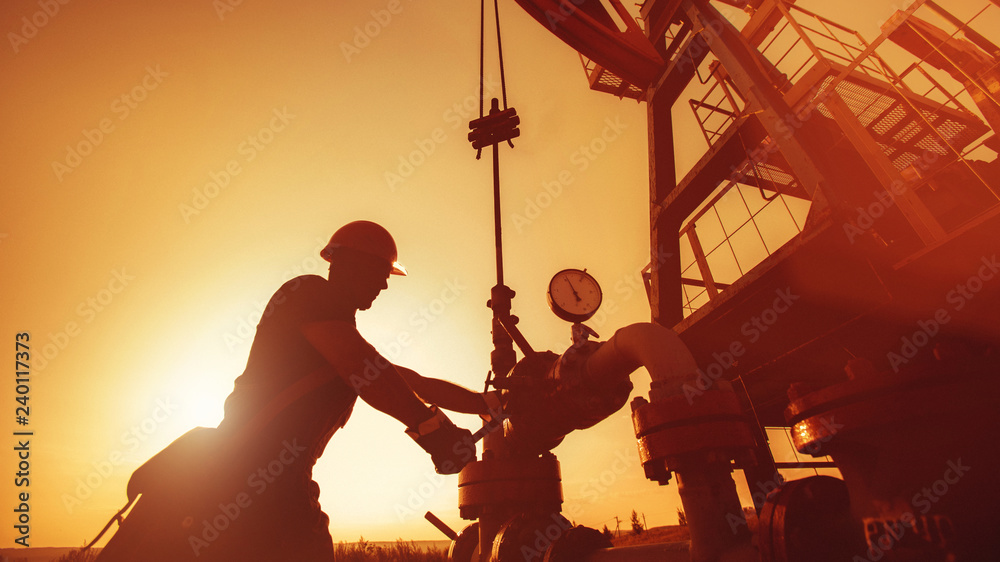 Oil worker is checking the oil pump on the sunset background. - obrazy, fototapety, plakaty 