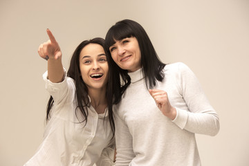 Wall Mural - A portrait of a happy mother and daughter at studio on gray background. Human positive emotions and facial expressions concept