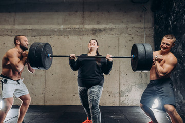 motivated plump girl is holding barbell with her male friends. friendship. friends who are ready to support you in any situation