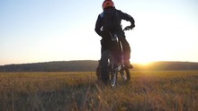 Biker Stopped At The Field To Wait For His Friend. Sportsman At The Meadow. Man Enjoying Ride On His Motorcycle. Beautiful Sunset At Background. Slow Motion Close Up Back View