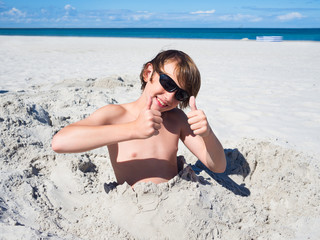 Teenager boy has fun digging in the sand at Baltic Sea