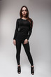 Young modern sexy brown-haired woman in a fashionable transparent t-shirt in black stylish pants and leather shoes on her heels posing indoors against a white wall. Beautiful girl