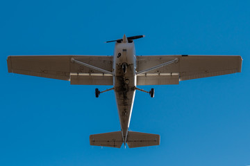 A small single engine airplane directly overhead. Blue sky above. Fast shutter to freeze propeller. Bottom of plane is dirty.