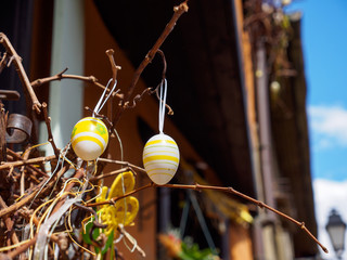 Closeup detail of two hand painted Easter eggs hanging off decorative tree branches. Shallow focus. Eguisheim, France. Travel and holidays.