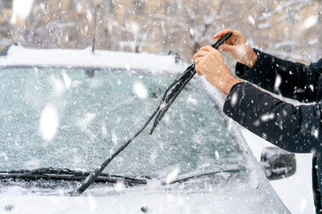 man adjusting and cleaning wipers of car in snowy weather b