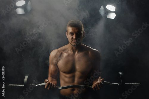 Fotografie, Obraz young man with a barbell posing on a dark background