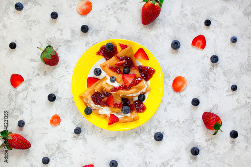 Fotografía Two thin pancakes, folded in triangles, are poured with sour cream, jam and decorated with fresh berries surrounded by blueberries and strawberries