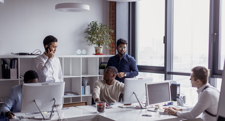 Canvas Print - Successful mixed race hipster male team in coworking space. Freelancers cooperate working in open space modern office