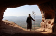 HERMIT  MAN LOOKING TO THE VALLEY FROM A HIGH CAVE WITH A BRANCH IN THE HAND IN SUMMER 