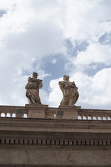 Vatican City, Italy, Rome - two stone statues on a marble balcony, dressed in robes with cloudy sky behind