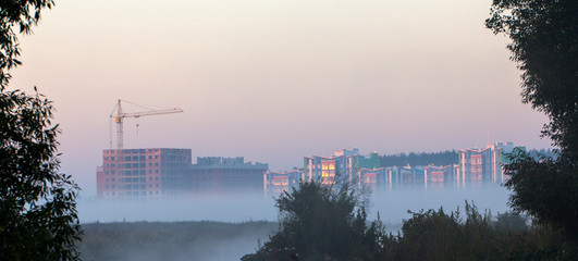 Wall Mural - very high construction crane in the morning fog, against the gray sky background