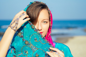 female model earrings and necklace in vacation on paradise tropical beach by ocean sea. hindu woman with kundan jewelry traditional India costume sari.girl near the rocks shores of Indian Ocean bay