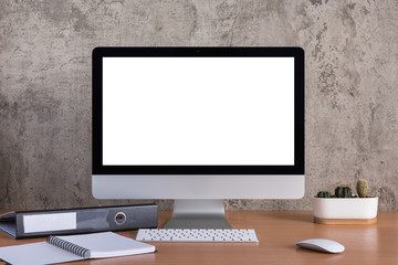 Blank screen of all in one computer with note book, pencil, document file and cactus vase on raw concrete background