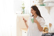 © Elena Kharichkina - Young woman using smartphone leaning at kitchen table with coffee mug and organizer in a modern home. Smiling woman reading phone message. Brunette happy girl typing a text message.