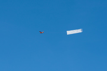 a small red airplane is pulling a white banner in the blue sky.