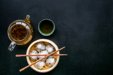 Chinese steamed dumplings Dim Sum in bamboo steamer with tea on black background top view mock up