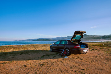 A car with opened trunk parked on the beach next to the sea on beautiful sunny morning